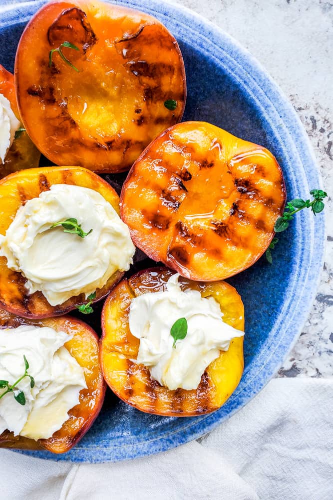 Overhead shot of grilled peaches on a blue plate. Some of the peaches are filled with mascarpone cheese.