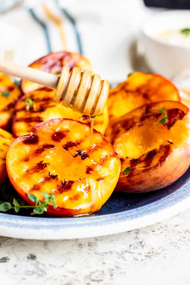 Cooked peaches on a blue plate with honey being drizzled over them.