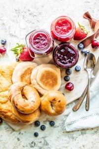 Shot of easy jam recipe in glass containers with bread products on a wooden cutting board.