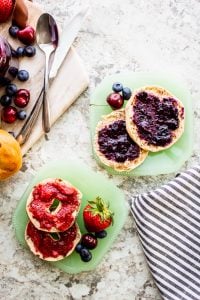 Overhead shot of jam on bagels on green plates on a white counter.