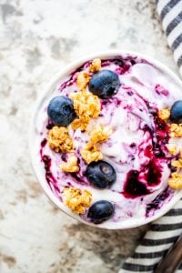 Shot of yogurt with jam and blueberries on top in a white bowl.