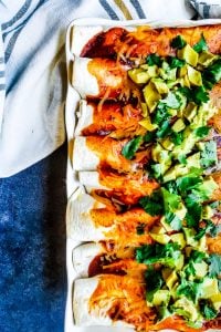 Overhead shot of enchiladas in a white baking dish with a white towel out of frame.