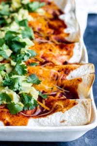 Shot of vegetarian enchilada in a white baking dish on a blue counter. 