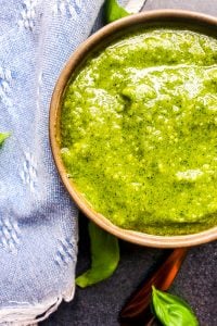 Overhead close up shot of pesto in a gray bowl with a blue napkin next to it.