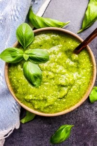 Overhead shot of basil pesto with gold spoon in the bowl and leaves surrounding it.