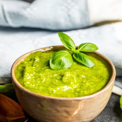 Basil pesto sauce in a gray bowl with a gold spoon next to it.