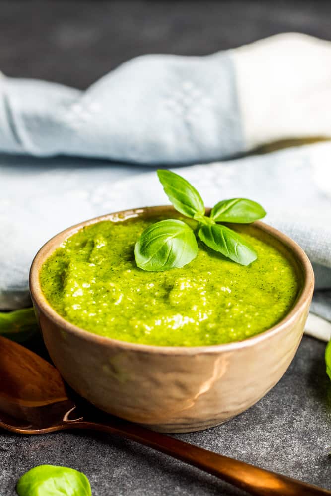 Basil pesto sauce in a gray bowl with a gold spoon next to it.