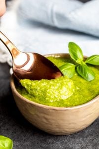 Gold spoon dipping into pesto sauce in a gray bowl.