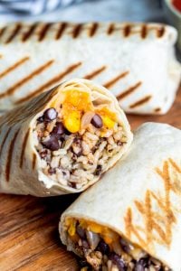 Burrito cut in half resting on top of another burrito on a wooden cutting board. 