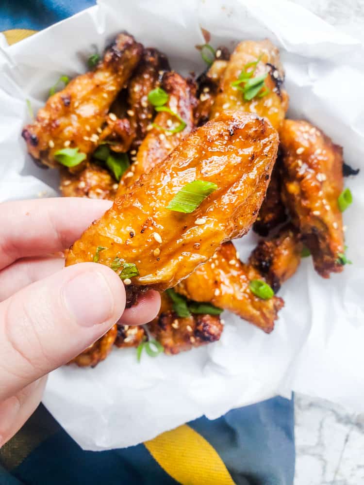 Hand holding chicken wing over bowl of wings.