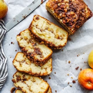 Apple bread laid out on white parchment paper and partially sliced.