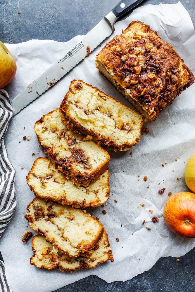 Apple bread laid out on white parchment paper and partially sliced.