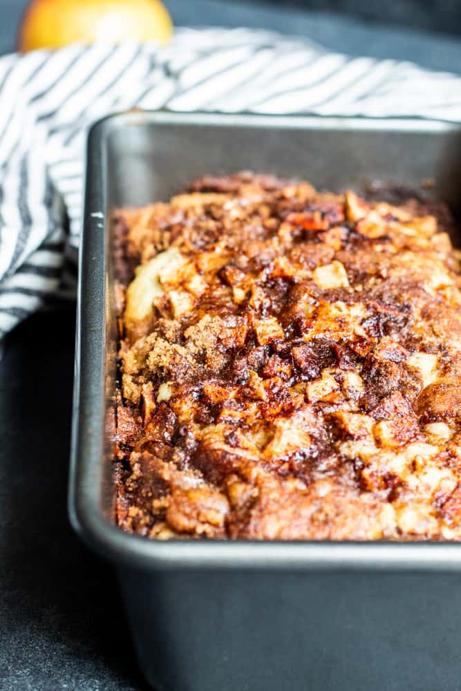 Apple Cinnamon bread in a dark gray loaf pan on a dark blue counter.