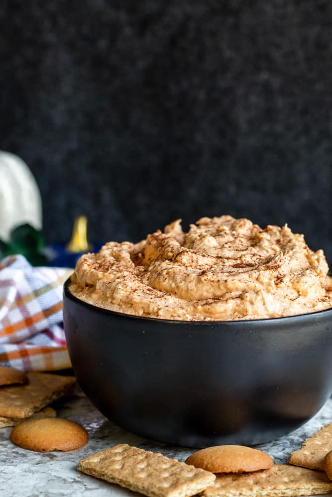 Far out shot of pumpkin dip in a black bowl on a white counter with wafers and Graham crackers.