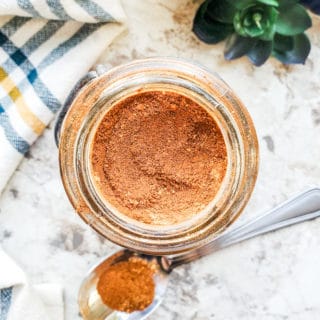 Overhead shot of pumpkin spice in a glass jar on a white counter with silver spoon next to it.