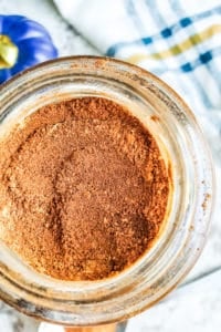 Close up overhead shot of homemade pumpkin spice in glass jar with striped towel next to it.