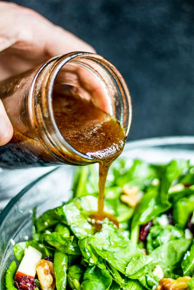 Vinaigrette Dressing being poured over spinach salad in a glass bowl.