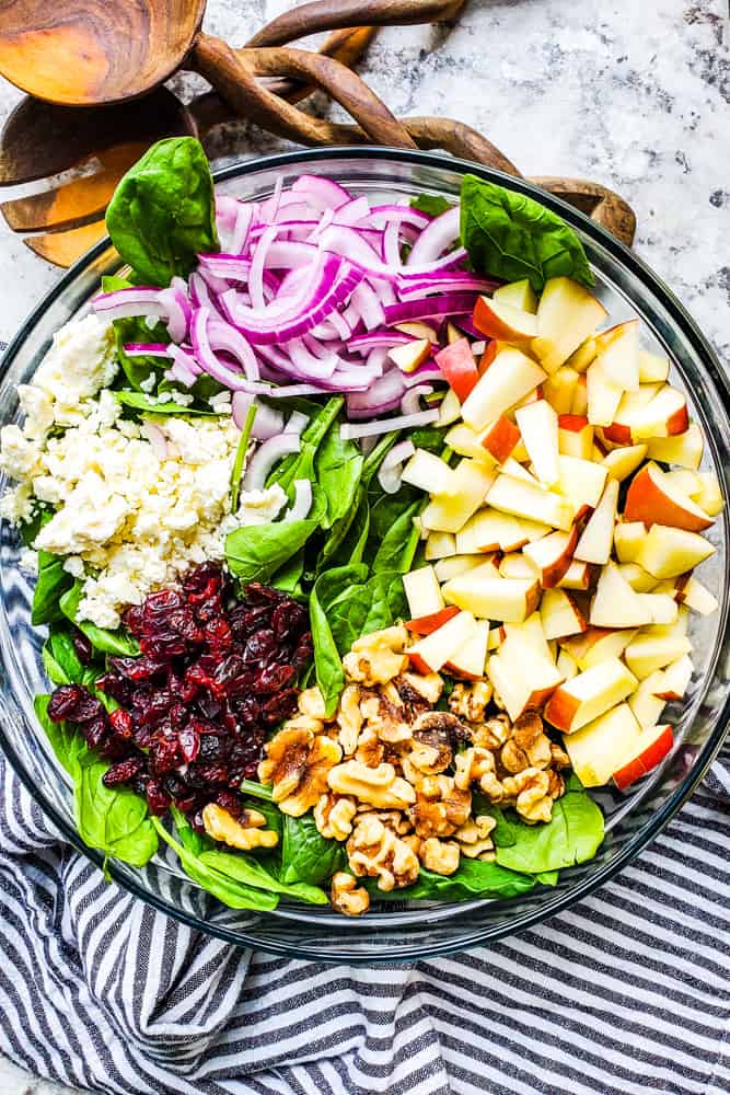 Salad ingredients all on top of salad in a glass bowl on a white counter.