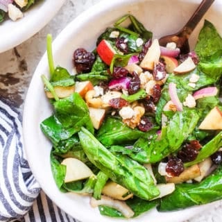 Salad in a white bowl with gold fork in it on a white counter.