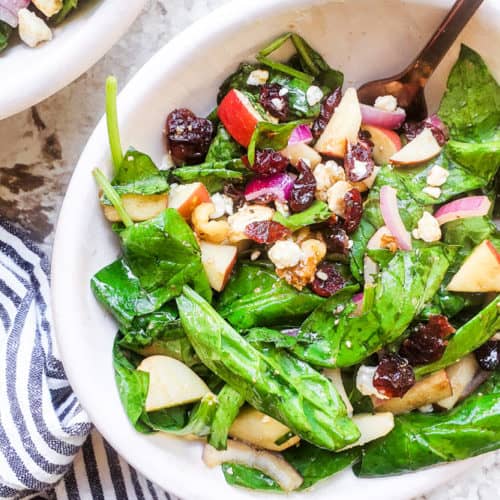 Salad in a white bowl with gold fork in it on a white counter.