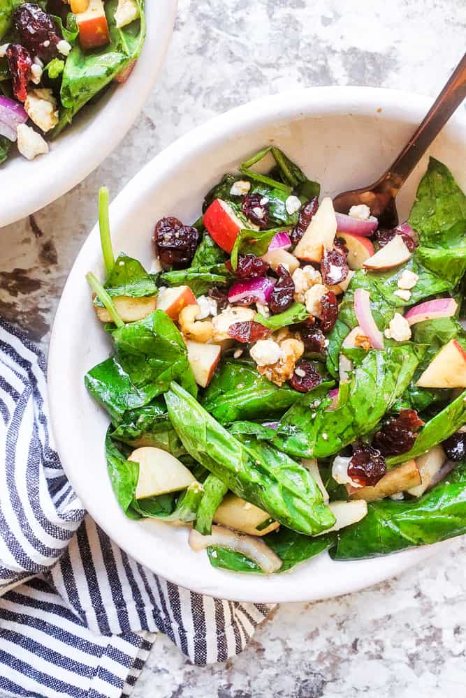 Salad in a white bowl with gold fork in it on a white counter.