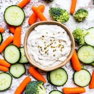 Ranch in a gray bowl with veggies surrounding it on a white counter.