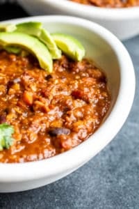 Close up shot of vegetarian chili recipe in a white bowl with avocados on top.