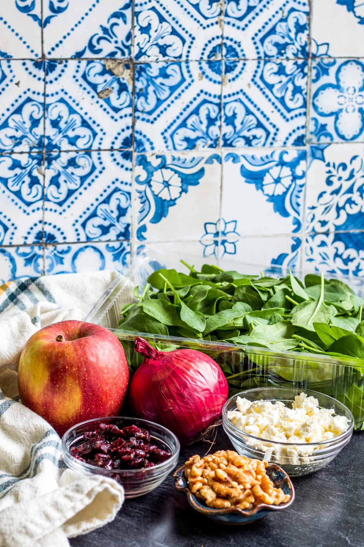 Spinach salad ingredients laid out on dark blue counter in bowls.