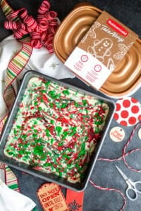 Sugar cookie fudge in a baking dish with gold container and holiday gifting supplies around it.