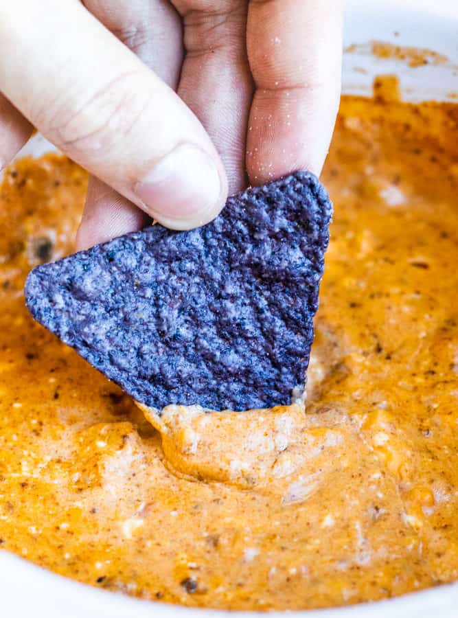 Hand dipping chip into chili cheese dip.