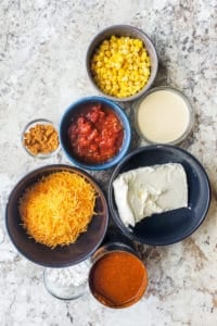Chili cheese dip recipe ingredients in bowls on a white counter.