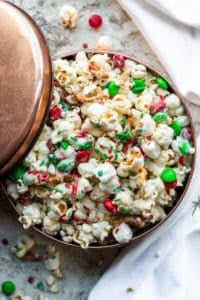 Overhead shot of Christmas Crunch mix in a copper tin on a white counter with napkin.