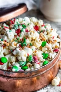 Christmas Crunch popcorn in a copper tin with lid resting on side on a white counter.