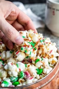 Hand reaching into tin of Christmas Crunch with mug in the background.