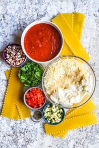 Vegetarian lasagna ingredients on a white counter in several different bowls.