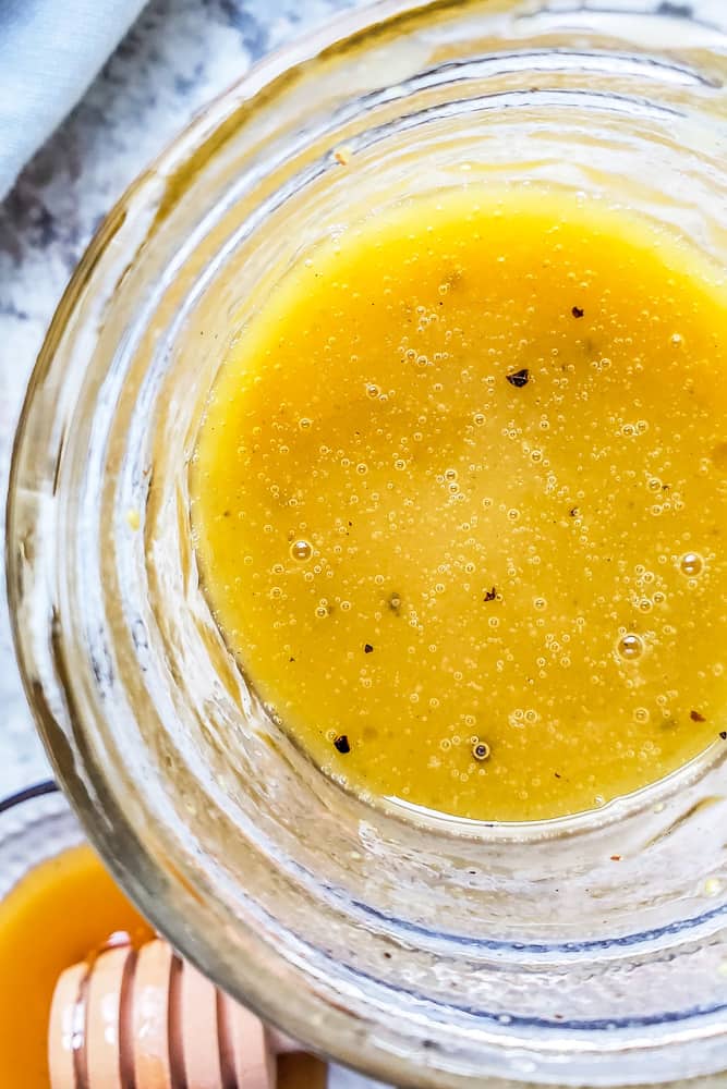 Overhead close up shot of honey mustard dressing in a glass mason jar on a white counter.