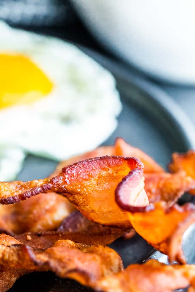 Close up of crispy bacon with egg in the background. 
