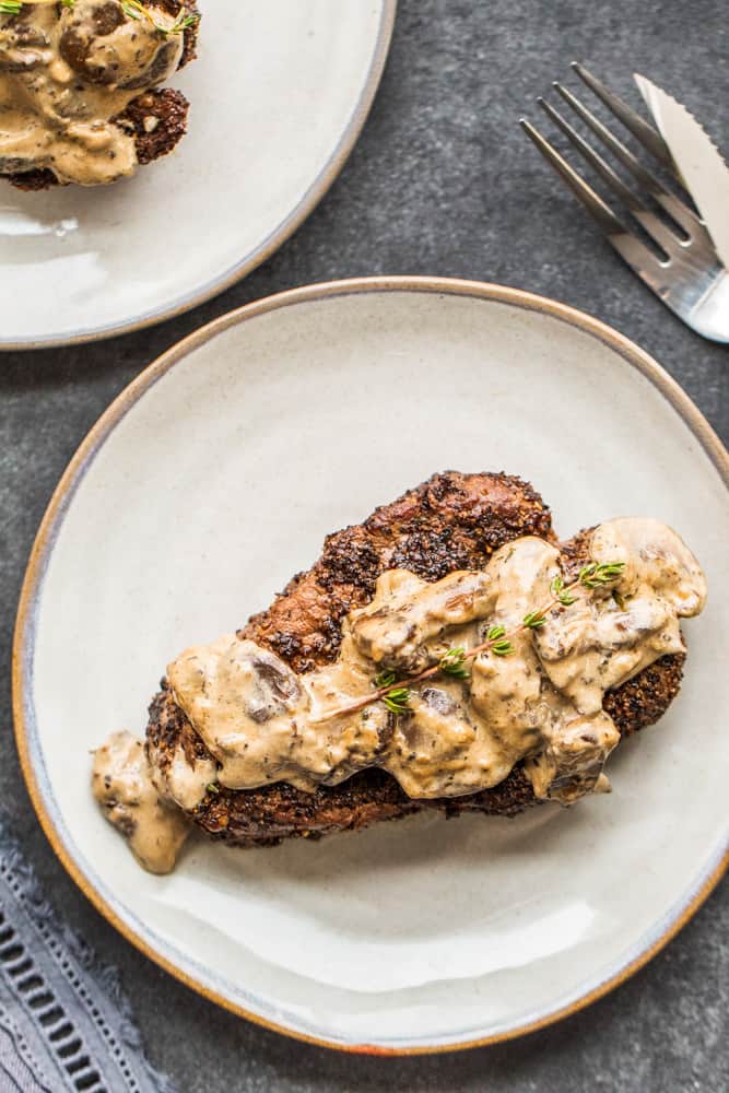 Overhead shot of two steak on gray plates with mushroom sauce on top.