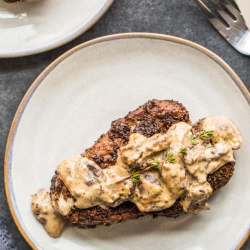 Pepper crusted steak on a gray plate on a blue counter.