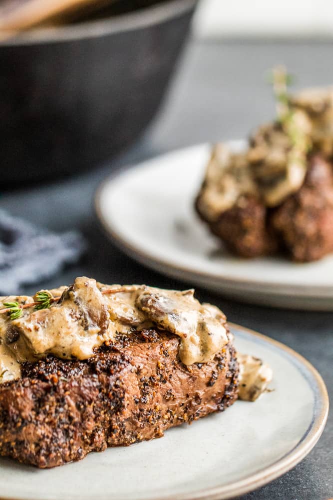 Steak on a gray plate with second out of focus in the background.