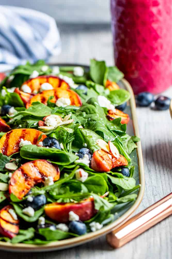 Grilled peach salad on a platter with pink dressing in the background.