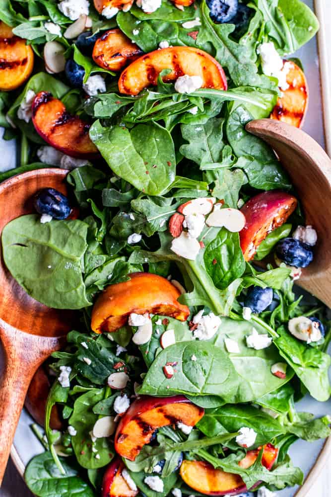 Salad on a blue platter with wood salad tossers. 