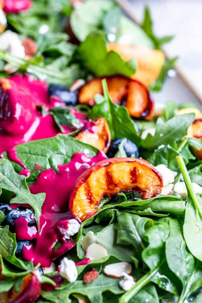 Close up shot of peach on top of salad with dressing.