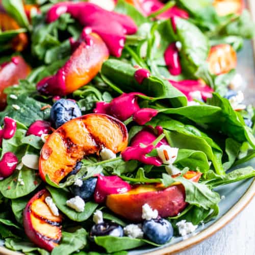 Grilled peach salad on a platter on a white counter.