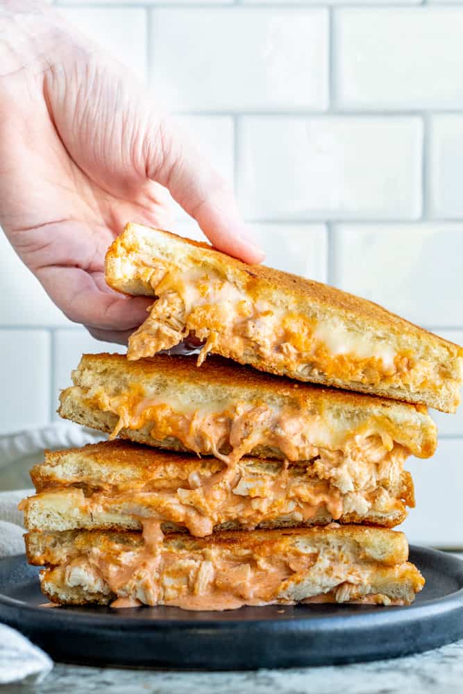 Hand picking up buffalo grilled cheese from stack on a black plate.