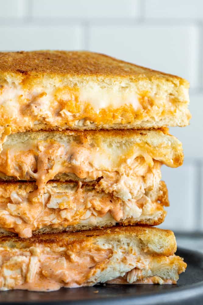 Buffalo chicken sandwiches stacked four high on a black plate with white background.