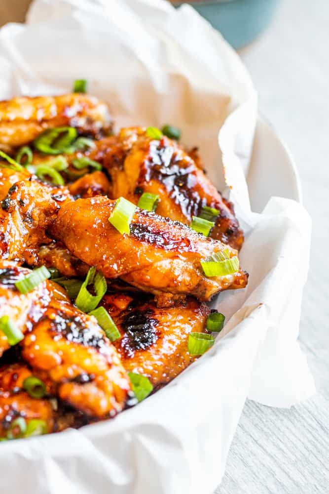 Grilled chicken wings in a white bowl on a white table.