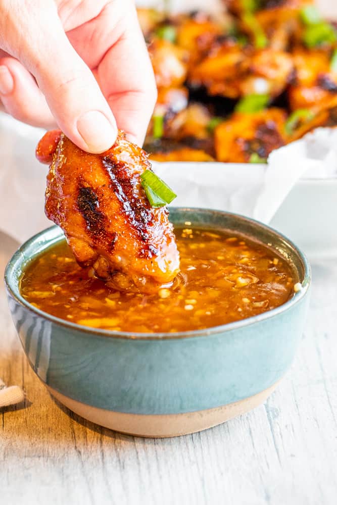 Hand dipping grilled chicken wing into sauce in a blue bowl on a white counter.