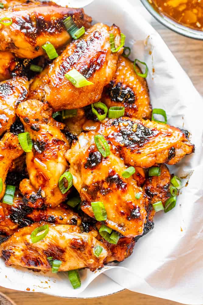 Overhead shot of chicken wings in a white bowl with peach sauce on the side.