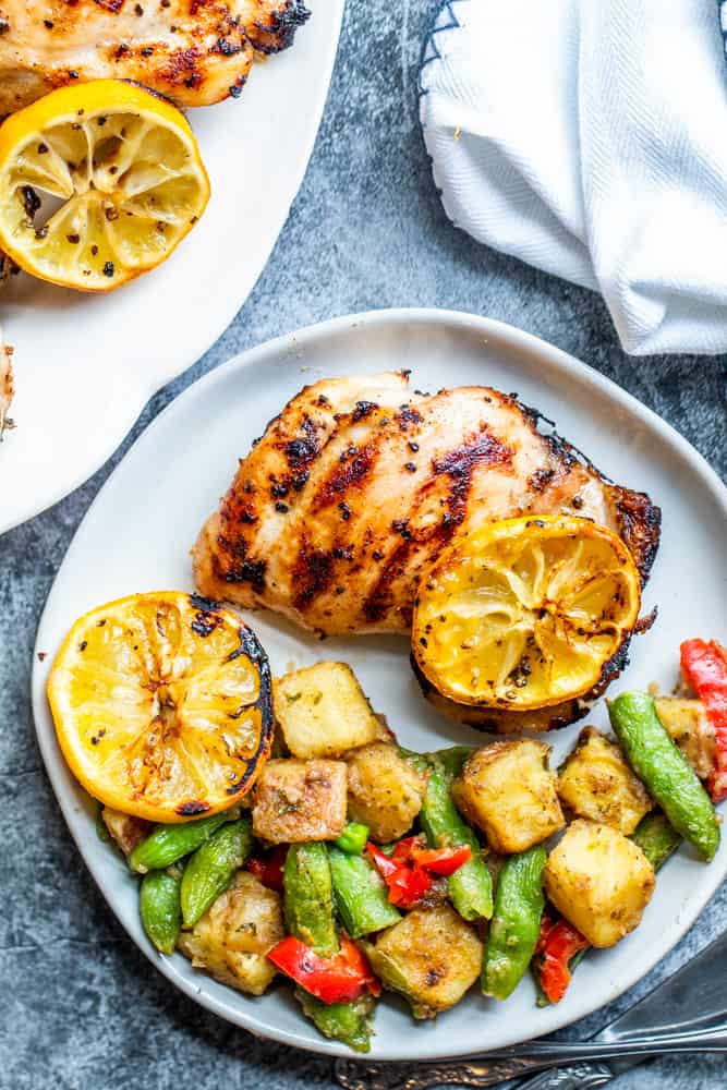 Chicken thigh on white plate on a blue counter with veggies on the side.